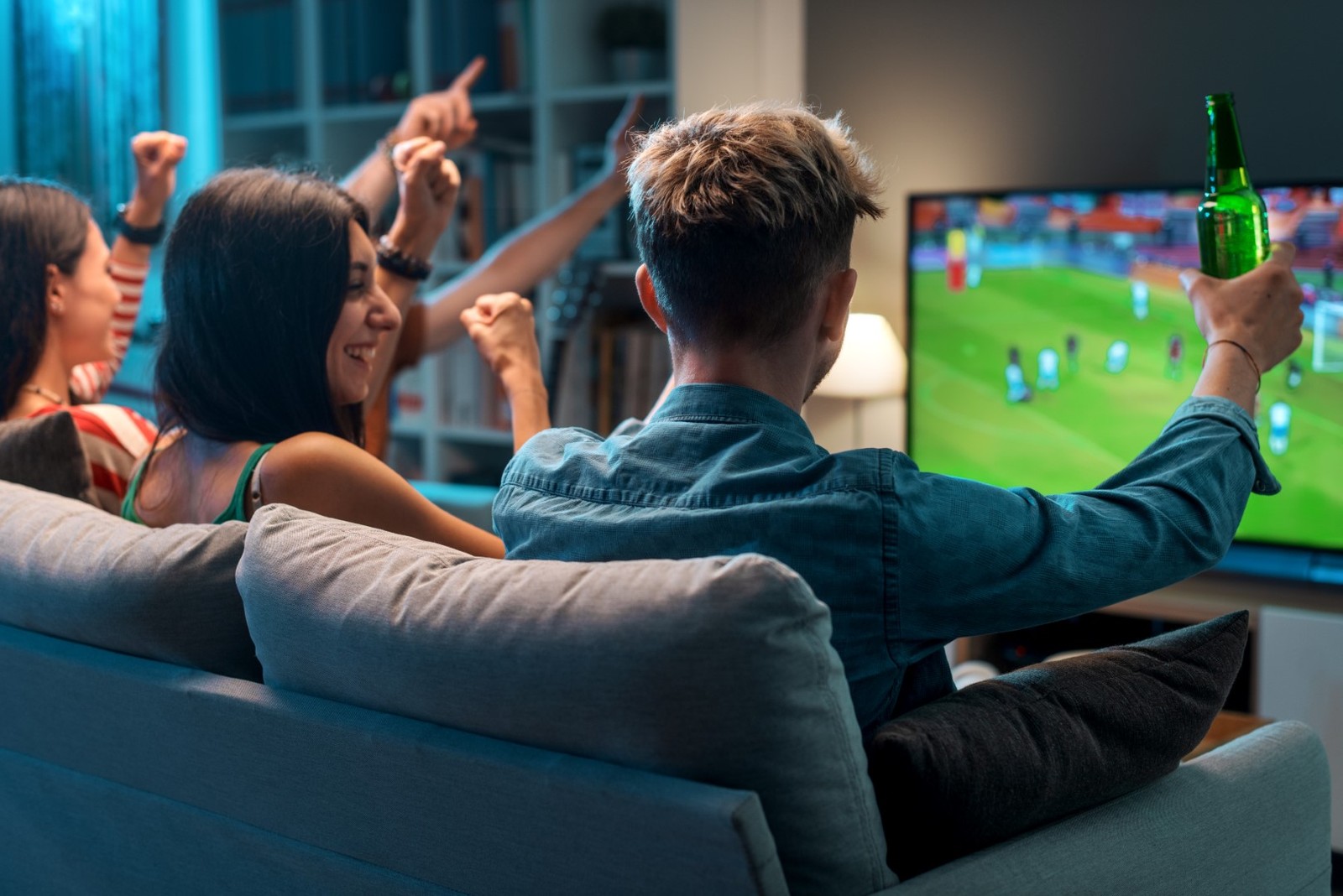 Group of young friends watching a football match on TV together and cheering for their team
